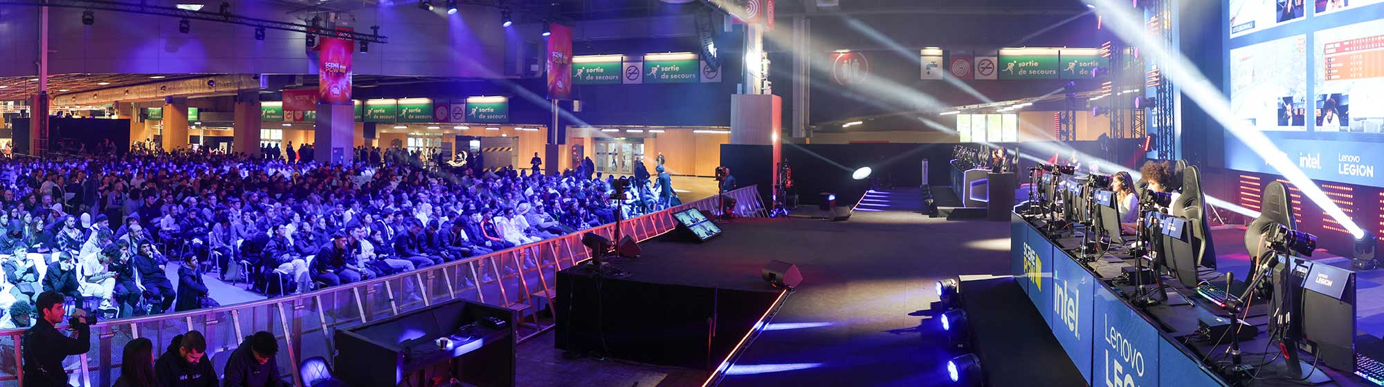 Une foule assise regarde des joueurs jouer à des jeux vidéo sur une scène dotée d'un écran géant
