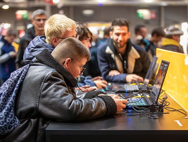 Focused children playing video games on laptops with an adult in the background