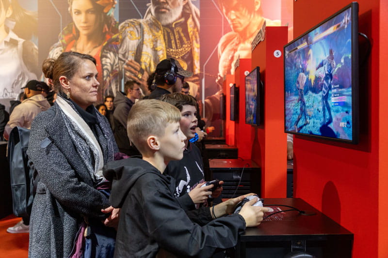 Parent et enfants partageant un moment ensemble sur le jeu vidéo Tekken 8 à la Paris Games Week 2023